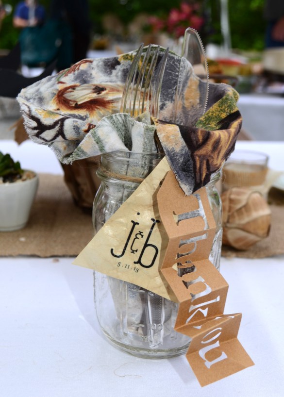 At each place setting, sat a mason jar containing a napkin and eating utensils. The mason jar also sports two hand made tags. One die cut tag that says thank you and another with the couple's custom monogram and the date on one side and on the other another little note that reads: 